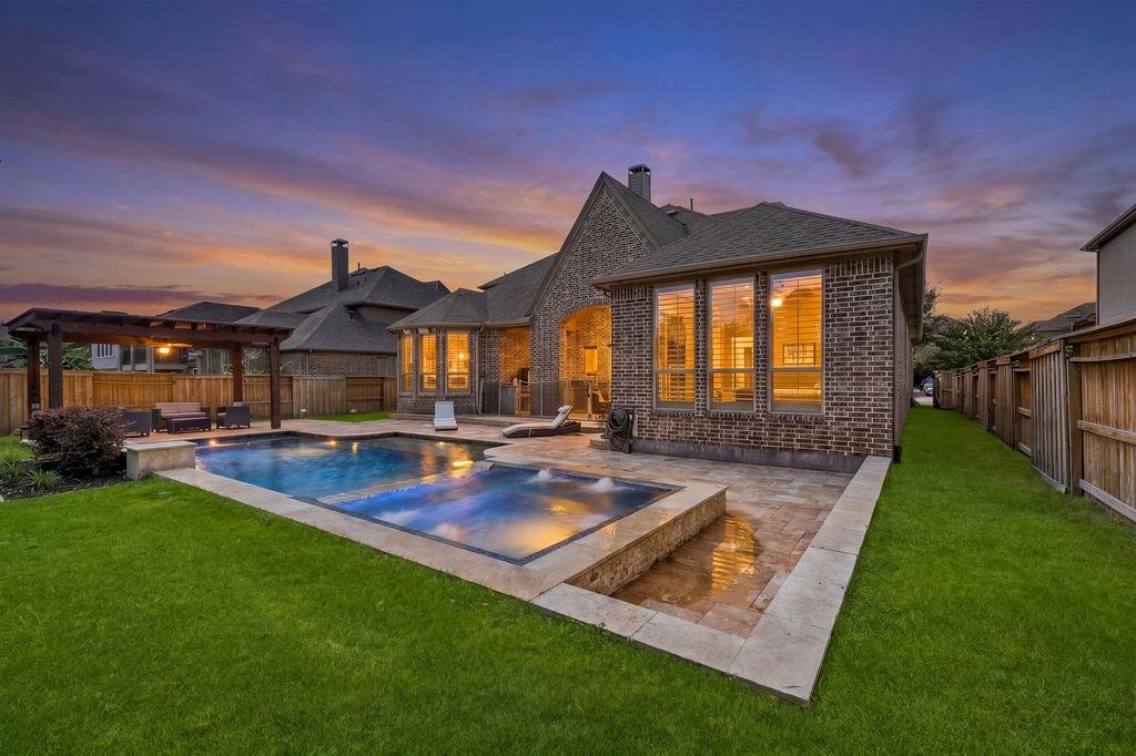 Rear brick exterior with illuminated windows, a swimming pool, and covered patio at dusk.