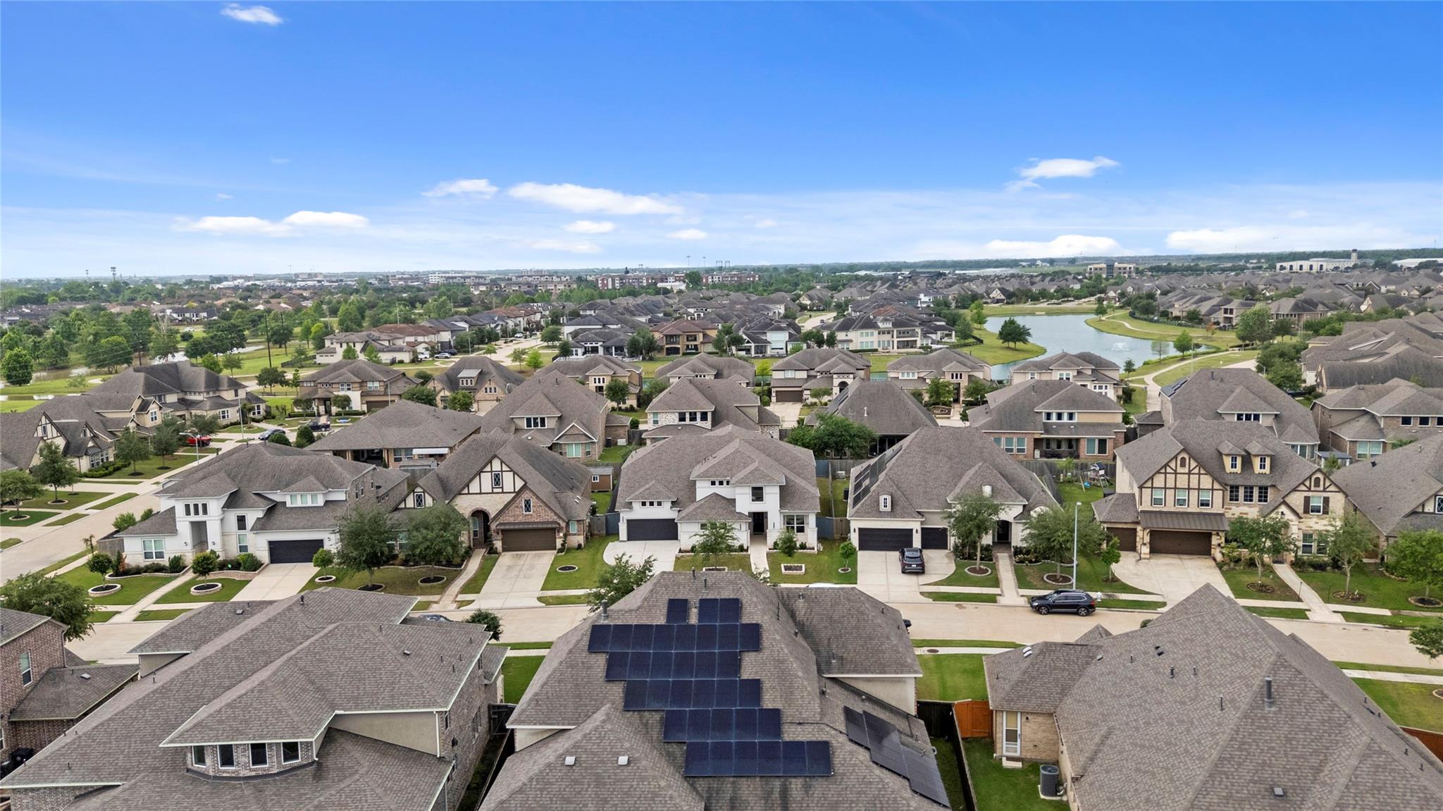 Aerial view of a suburban neighborhood with a pond and homes with rooftop solar panels.