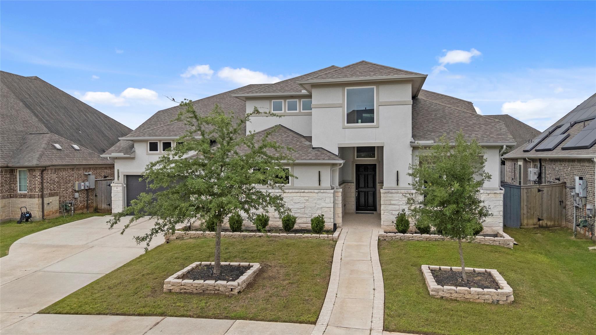 Two-story light-colored home with a stone facade, landscaped lawn, and broad driveway.