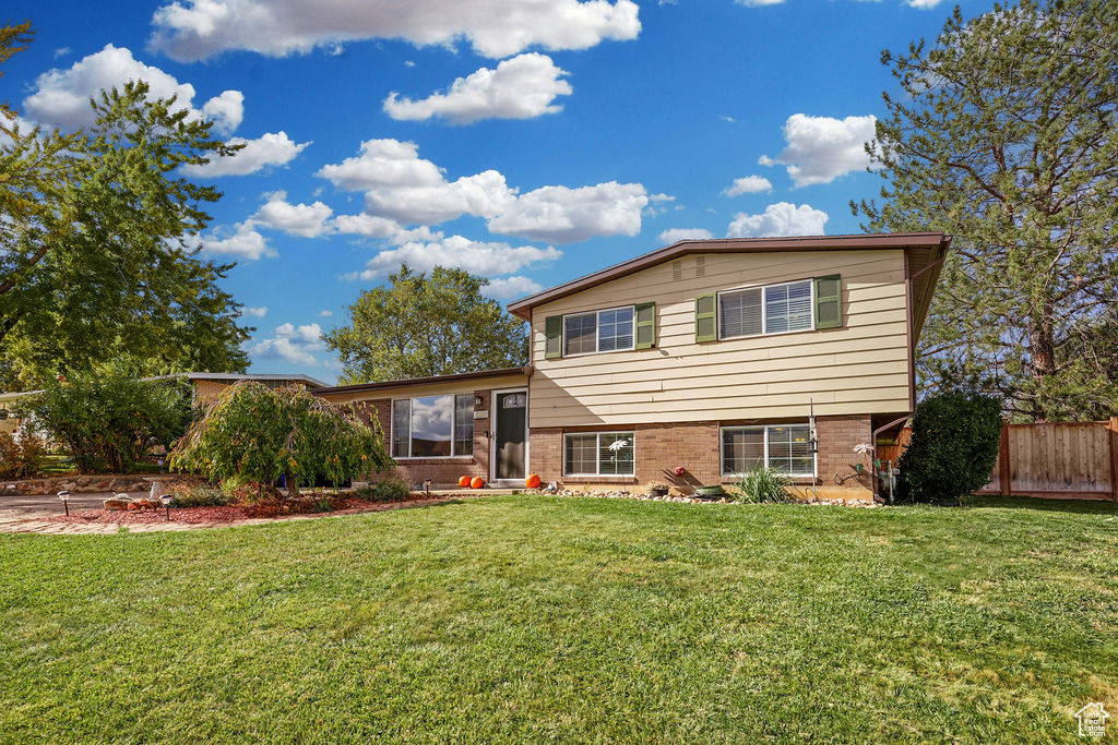 Split-level home with beige siding and brick facade, set behind a broad lawn and mature trees.