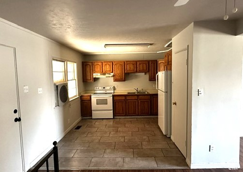 Empty kitchen with dark wood cabinets, white appliances, and large square tile flooring.