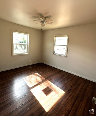 Vacant bedroom with dark wood floors, two windows, and sunlight streaming across the floor.