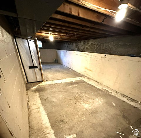 Unfinished basement with exposed ceiling joists, concrete walls, and a narrow door.