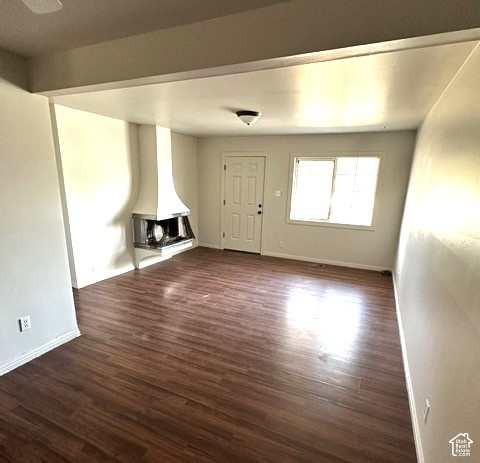 Empty living room with dark flooring, a white corner fireplace, and a window beside the front door.