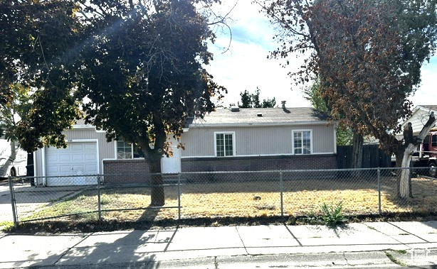 Single-story house with attached garage behind a chain-link fence and mature trees.