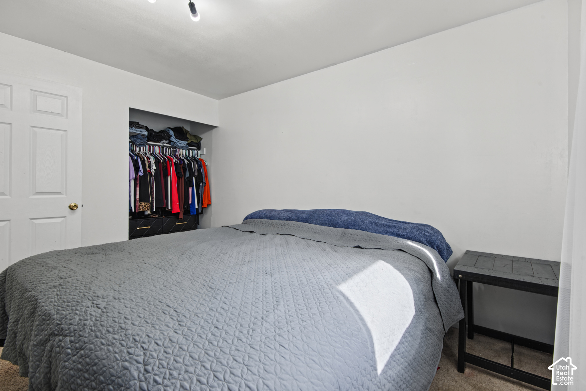 Bedroom with a gray quilted bed, blue blanket, and open closet filled with clothes.