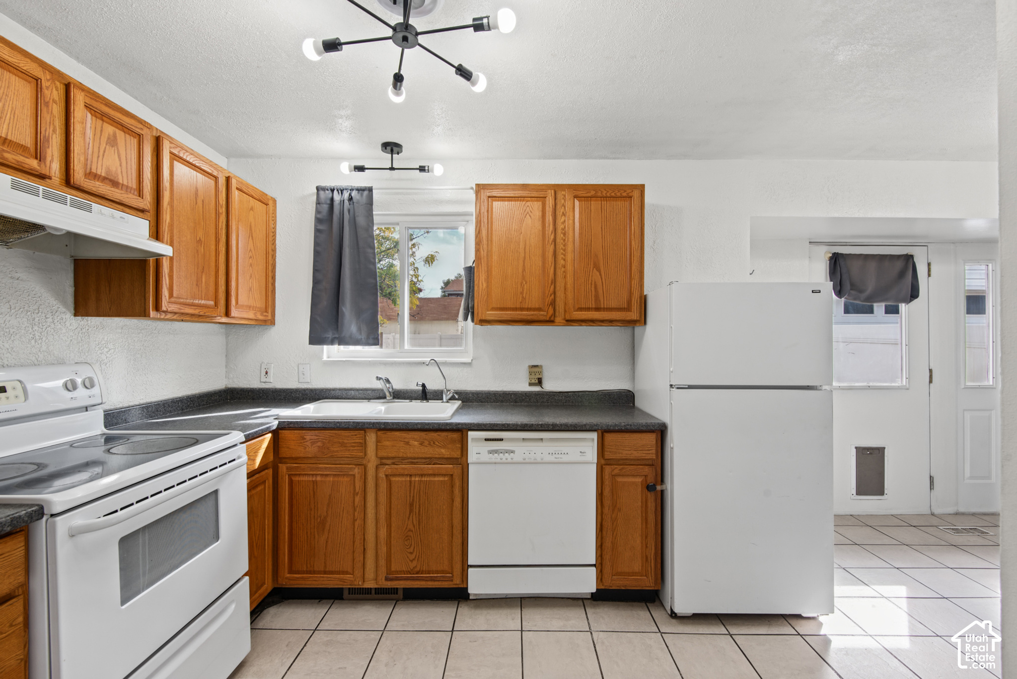 Kitchen with oak cabinets, dark countertops, white appliances, and a window above the sink.