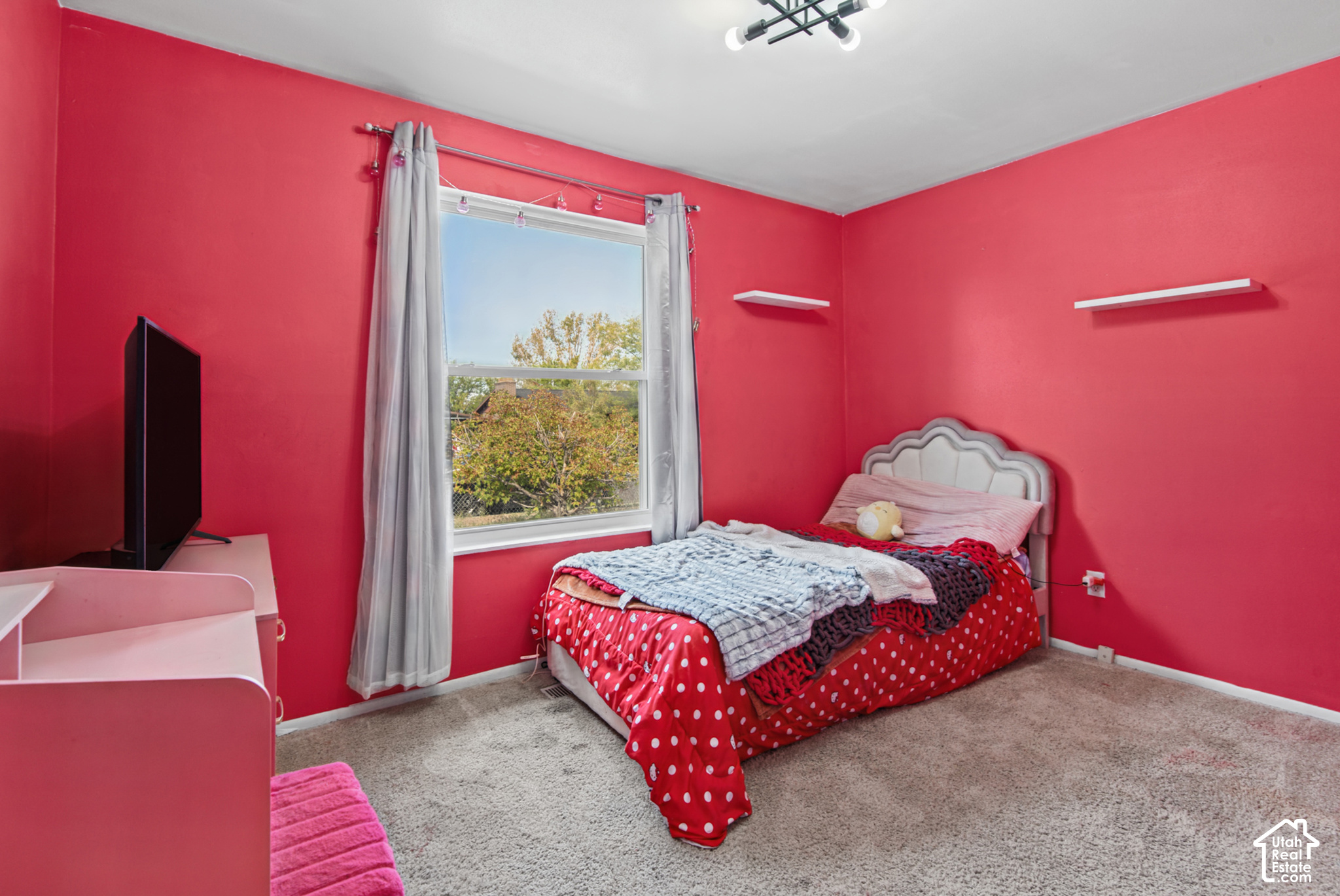 Bedroom with vivid red walls, a bed with red polka-dot bedding, and a window framed by gray curtains.