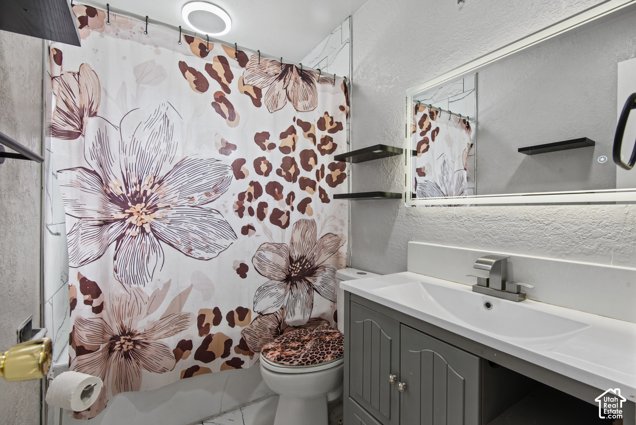 Bathroom with a gray vanity, large mirror, and bold floral-patterned shower curtain.