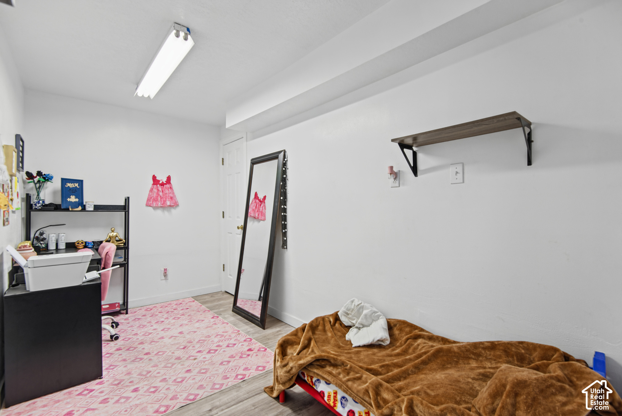 Bedroom with a low bed, brown blanket, pink patterned rug, and full-length mirror.