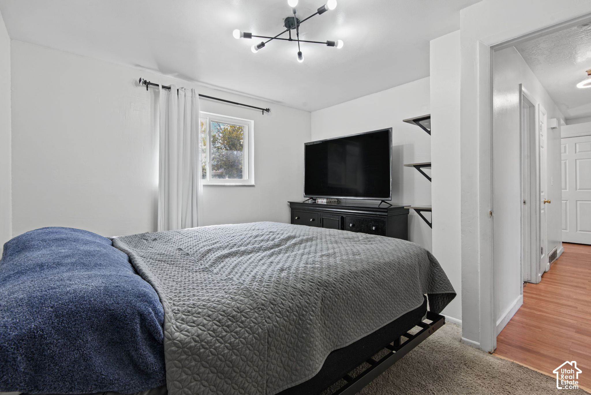 Furnished bedroom with a gray-quilted bed, blue blanket, and television on a dark dresser.