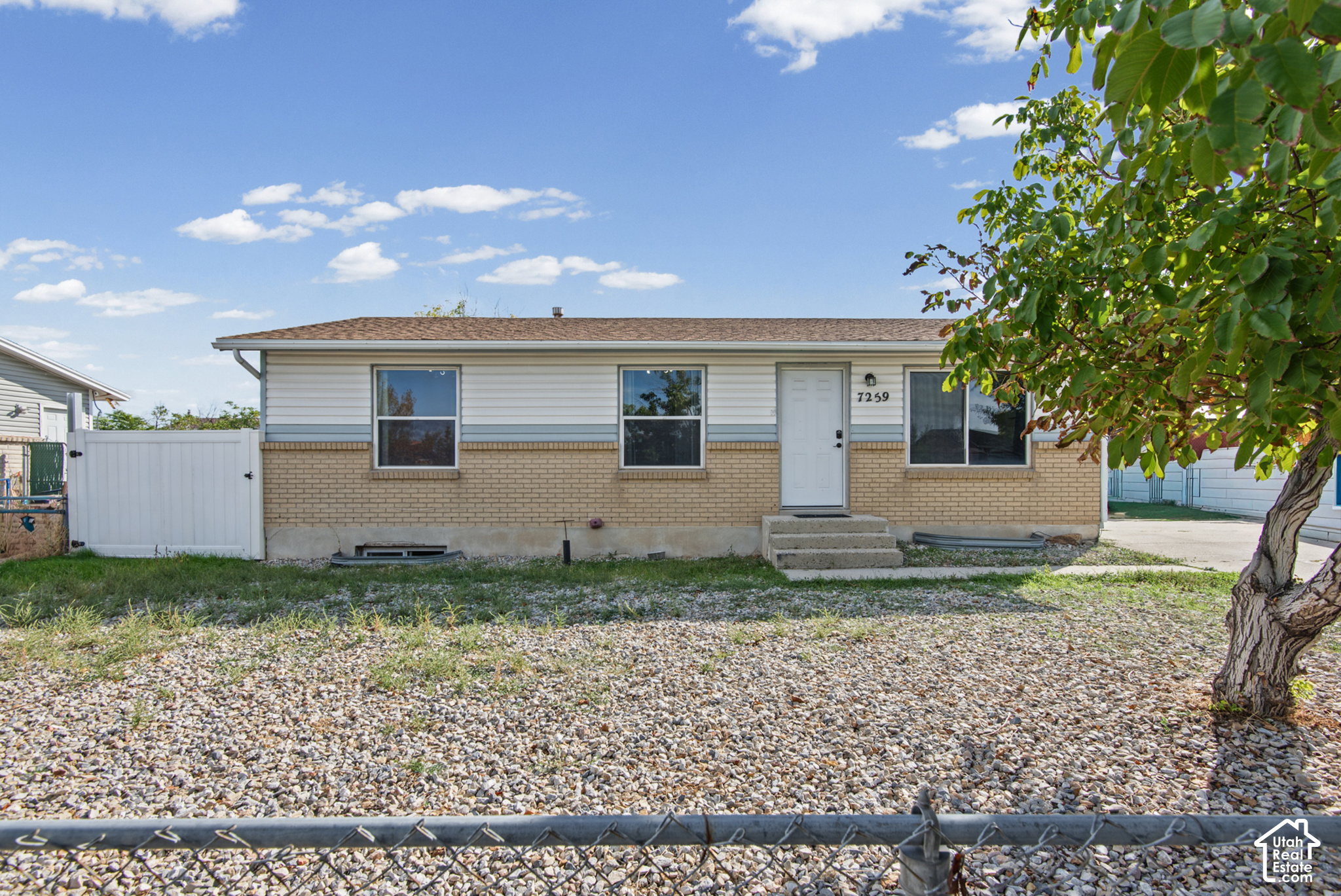 Single-story white-and-tan brick house with a gravel yard and chain-link fence.