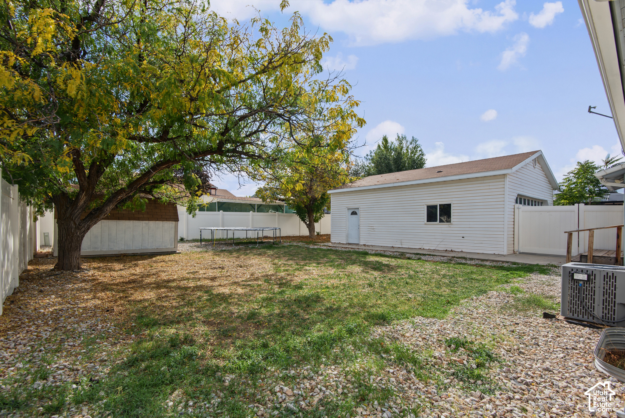 Backyard with a white detached garage, gravel landscaping, and a large tree.