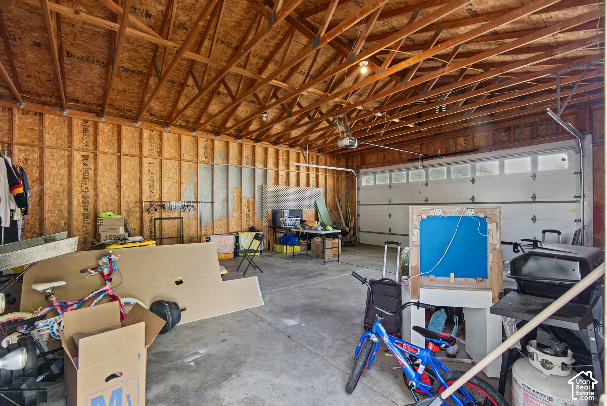 Garage with exposed roof trusses, a wide windowed door, bicycles, boxes, and stored belongings.