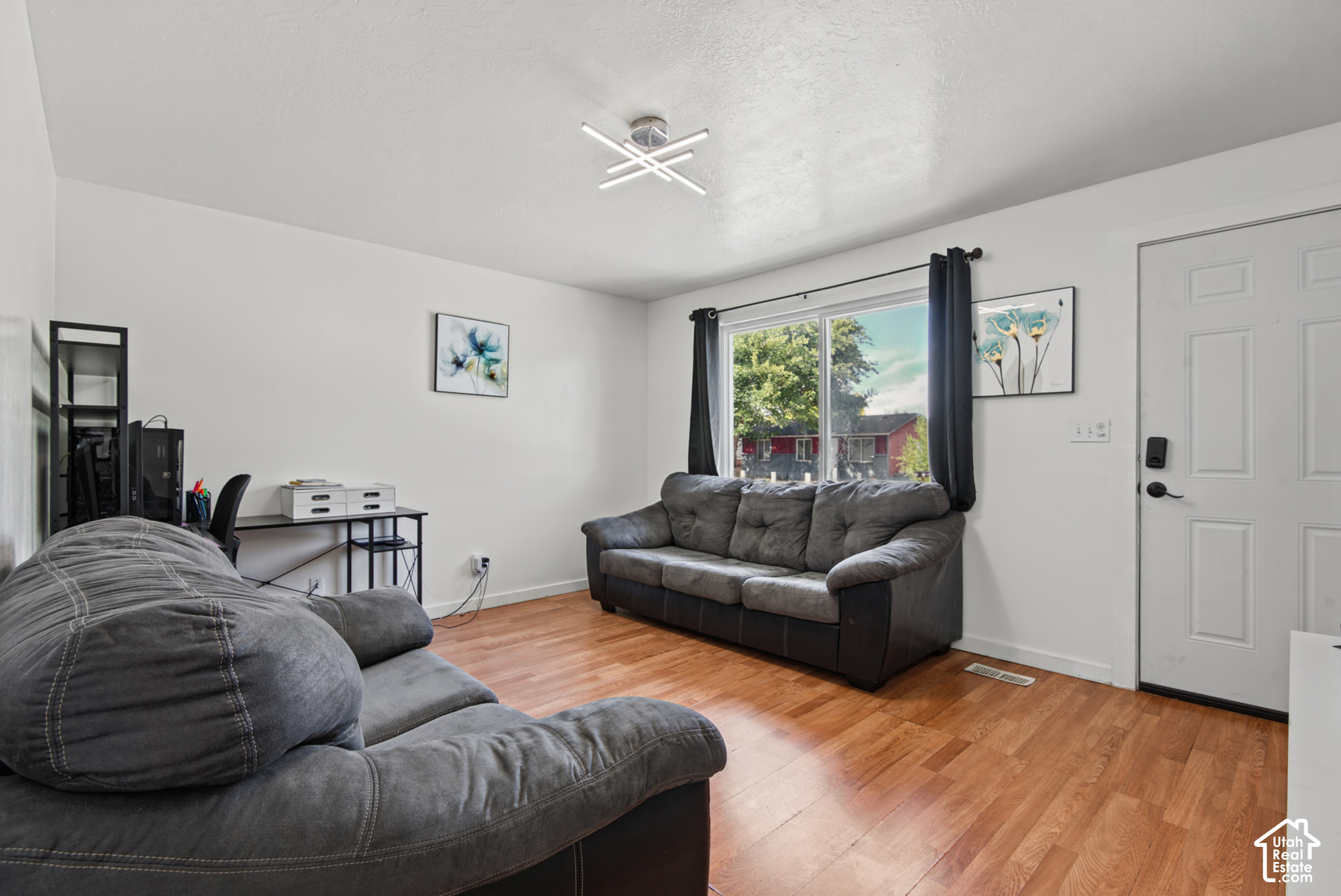 Living room with gray sofas, warm wood-look flooring, and a large curtained window.