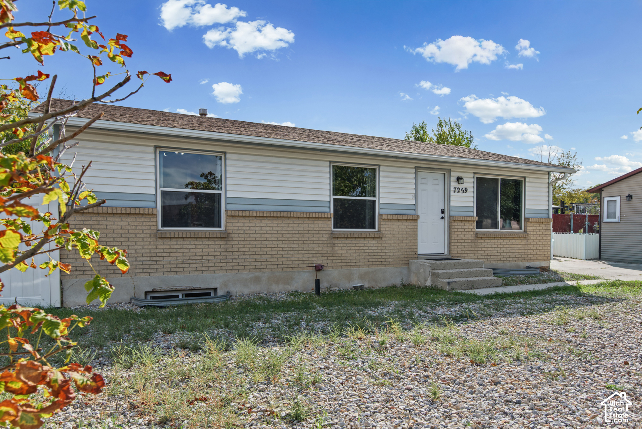 Single-story house with tan brick, white siding, and a gravel front yard.