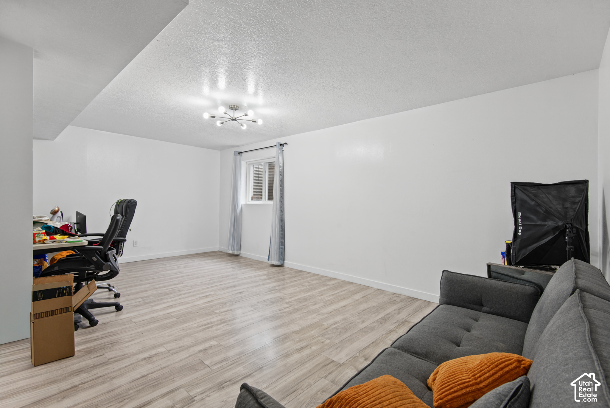 Finished room with light wood-look flooring, gray sofa with orange cushions, and a desk with gaming chairs.