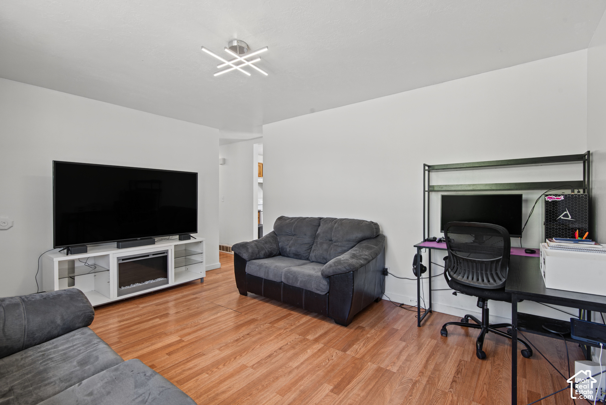 Living room with gray sofas, wood floors, a large TV, and a computer desk.