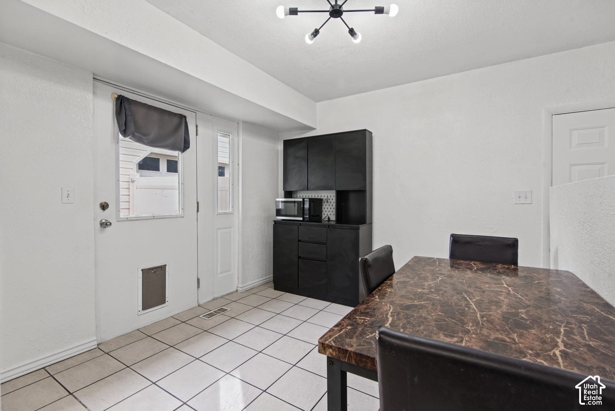 Dining area with a marble-look table, black chairs, tiled floor, and tall black cabinet.