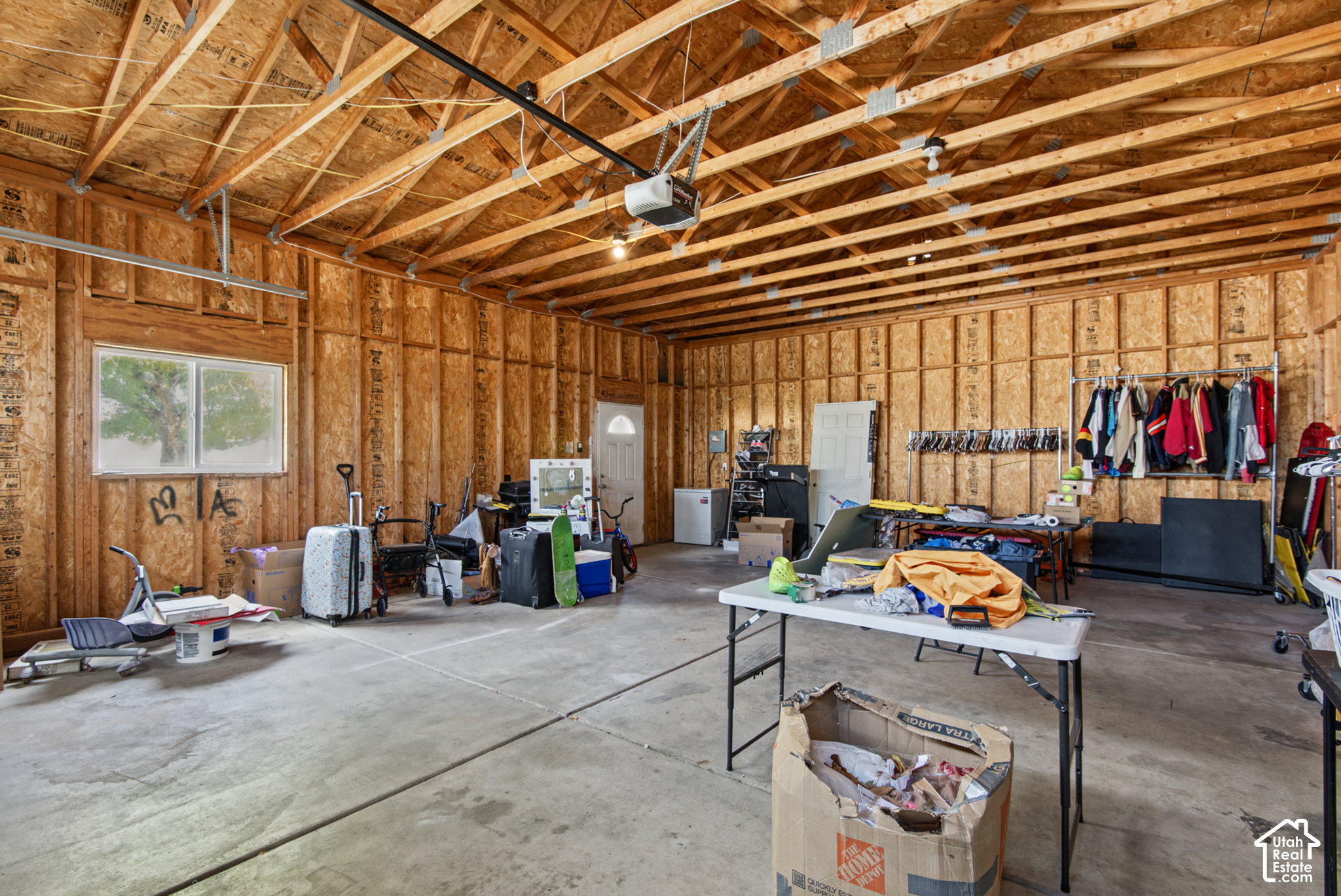 Large garage with exposed wood framing, concrete floor, storage racks, and a folding table.