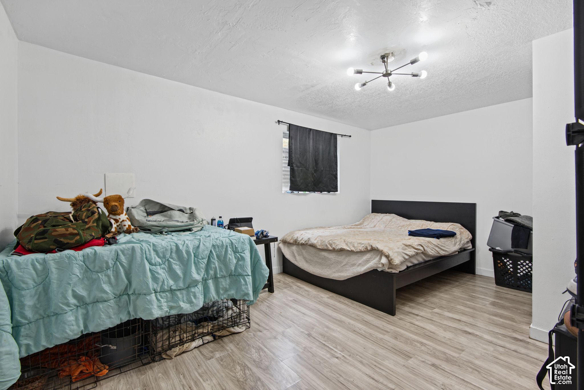 Bedroom with two beds, a black platform bed, turquoise bedding, and light wood-look flooring.