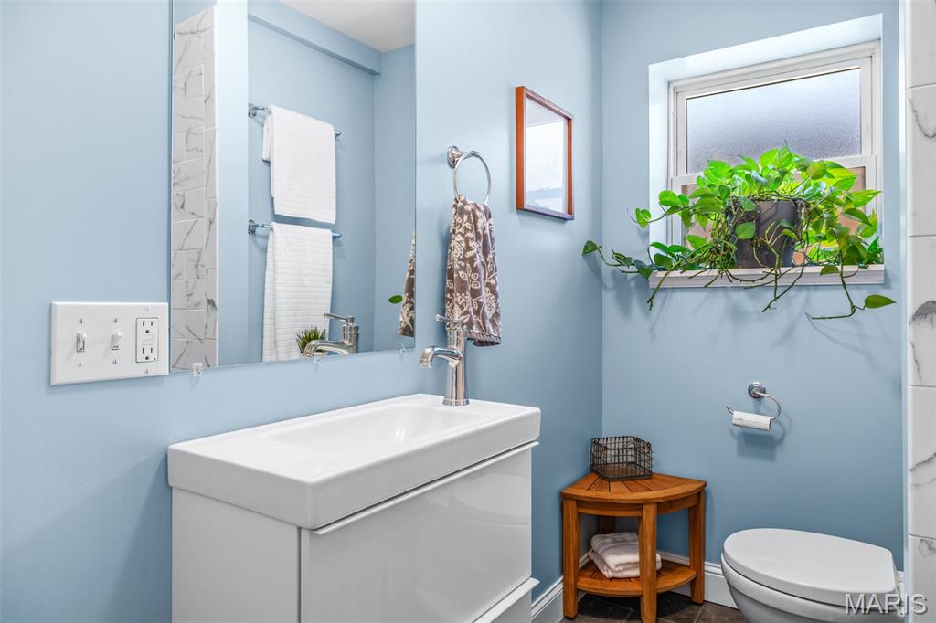 Bathroom with blue walls, white vanity and toilet, and a potted plant by the window.