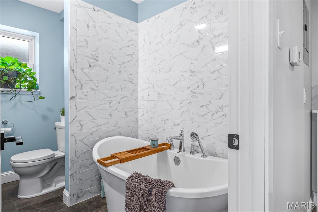 Bathroom with a freestanding tub, marble-look tile, and a frosted window beside the toilet.