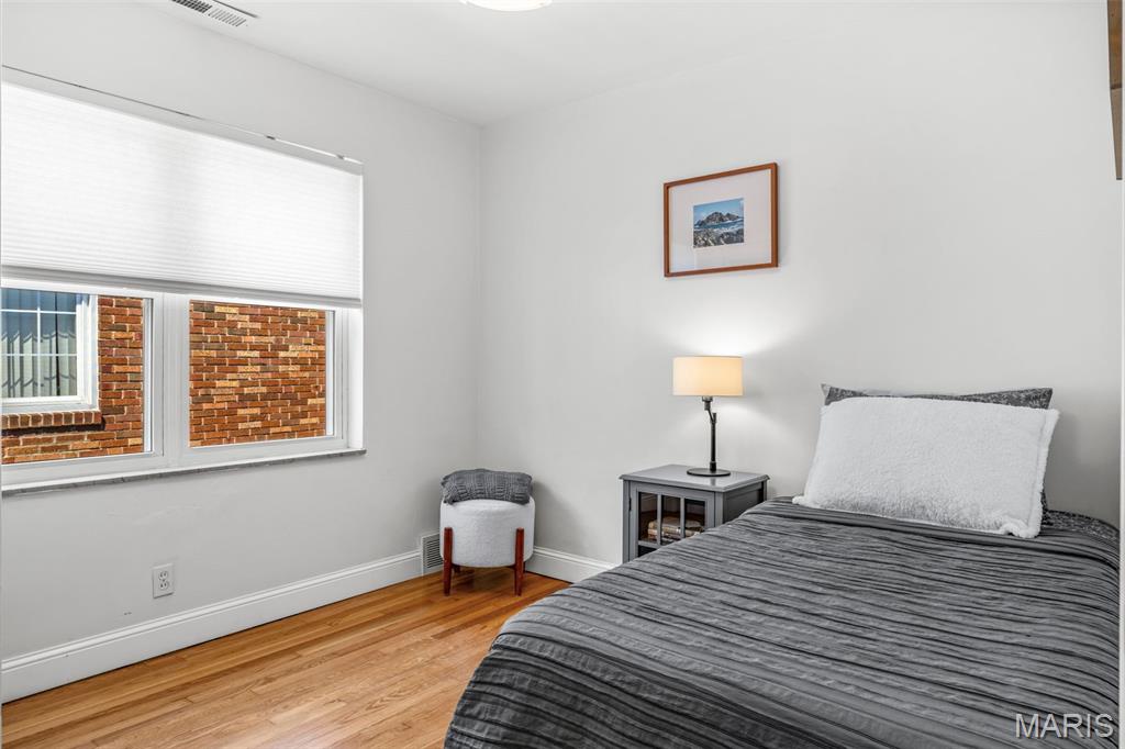 Bedroom with a gray-striped bed, bedside lamp, hardwood floor, and window with a white blind.