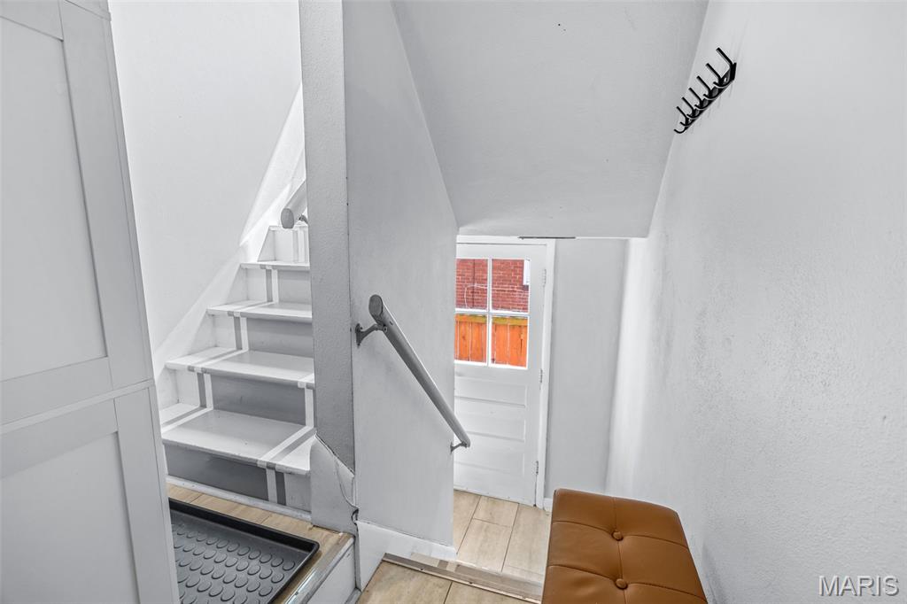 Entry stairway with white-painted steps, wall hooks, a brown bench, and a windowed door.