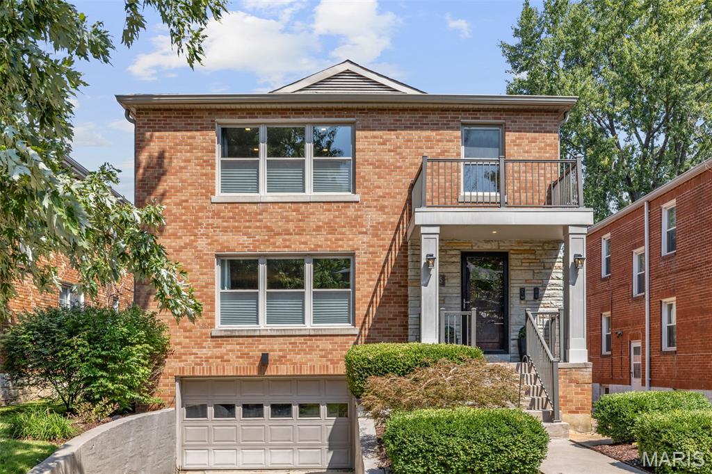 Two-story brick home with a second-floor balcony, raised entry, and attached garage.