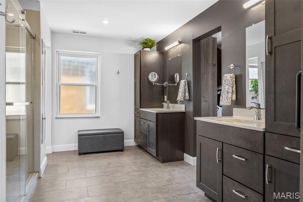 Bathroom with two dark wood vanities, a glass shower, frosted window, and tiled floor.