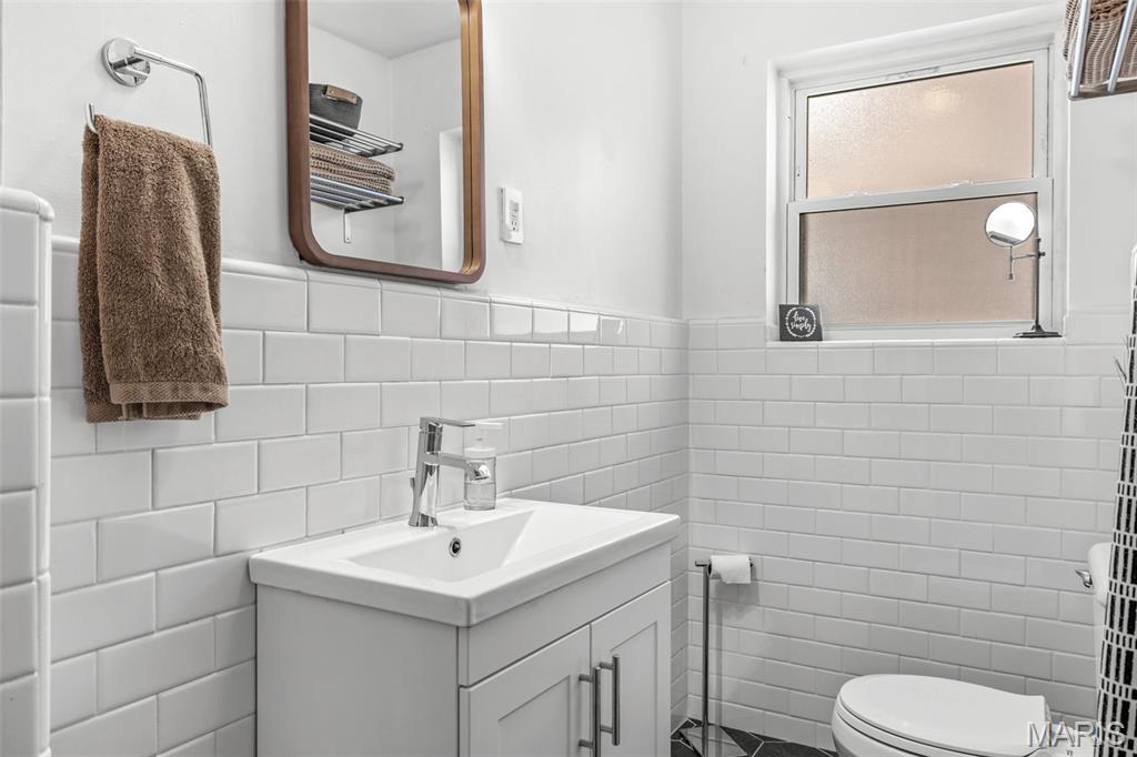 Bathroom with a white vanity, subway tile walls, and a high window.