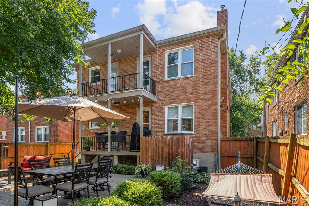 Red-brick home's rear exterior with a balcony, furnished patio, fenced yard, and hammock.