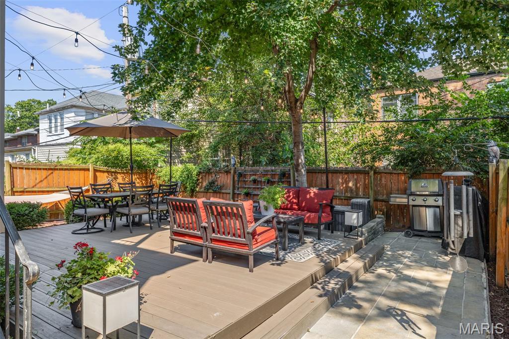 Furnished backyard deck with dining and lounge seating, shade umbrella, grill, and mature tree.