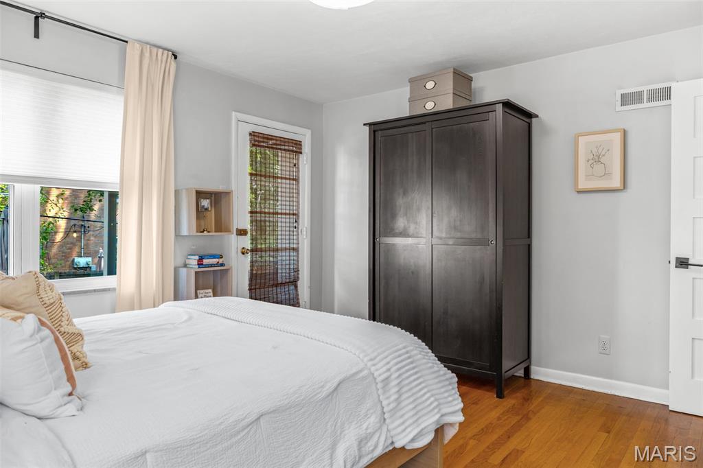 Furnished bedroom with a white bed, dark wardrobe, and hardwood floors.