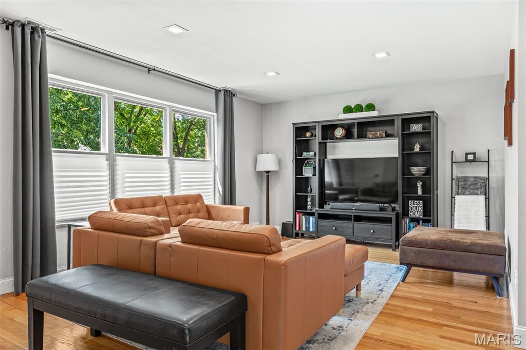 Living room with tan leather sofas, large curtained windows, hardwood floors, and a built-in TV cabinet.