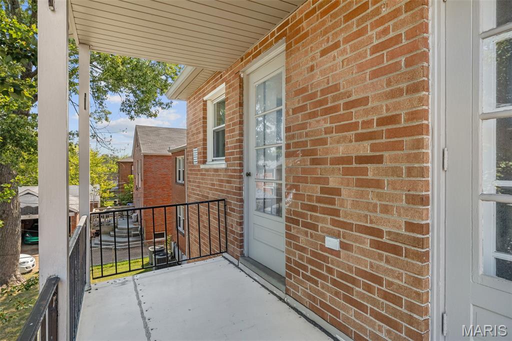 Covered balcony with brick walls, glass-paneled doors, and a black metal railing.