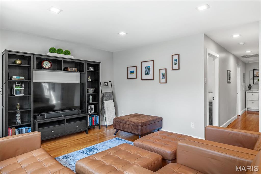 Living room with tan leather seating, blue-and-white rug, and a large television in built-in shelving.
