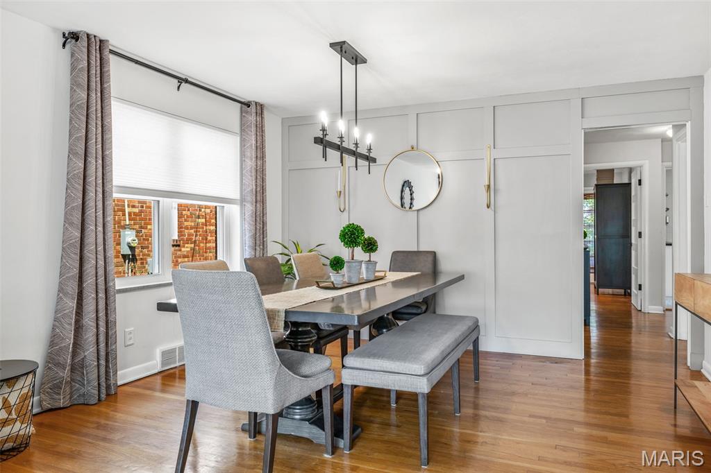Dining room with paneled walls, a long table, upholstered seating, chandelier, and hardwood floors.