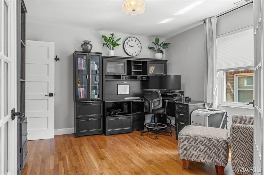 Home office with dark built-in desk and cabinetry, wood floors, and two upholstered chairs by a window.