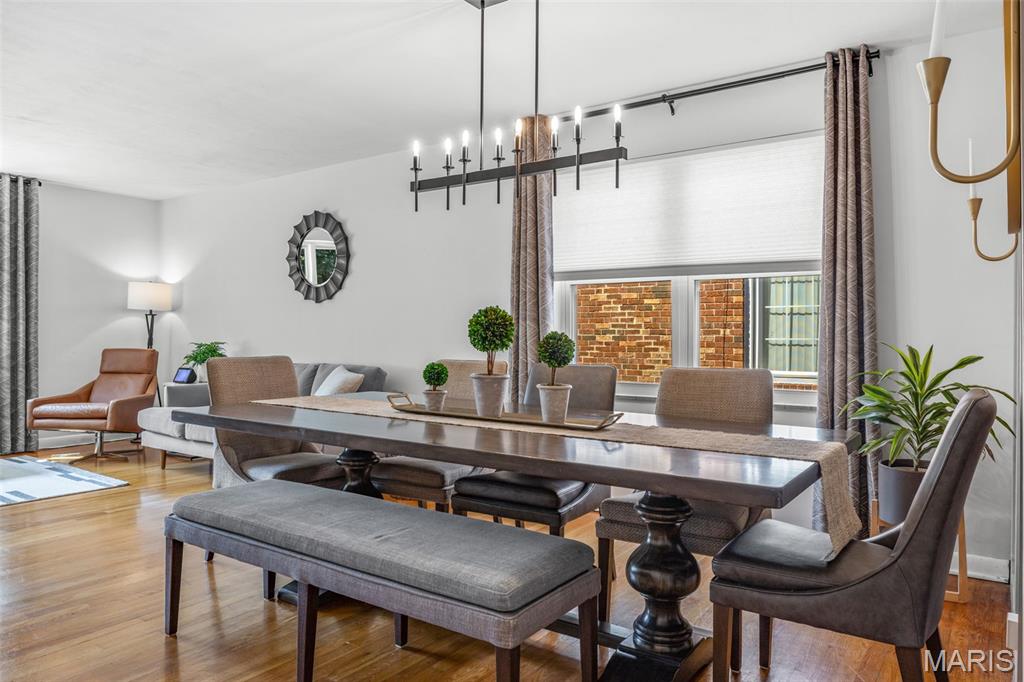 Dining area with a long dark wood table, upholstered seating, hardwood floors, and tall curtained windows.