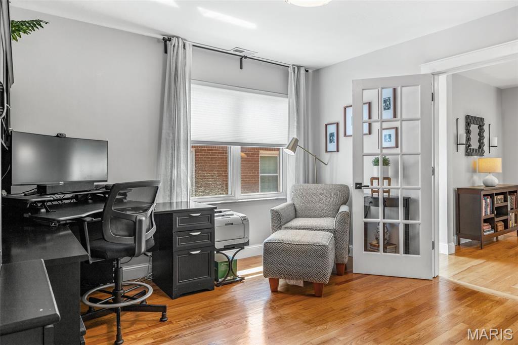 Home office with a black desk, window, patterned armchair, and hardwood floors.