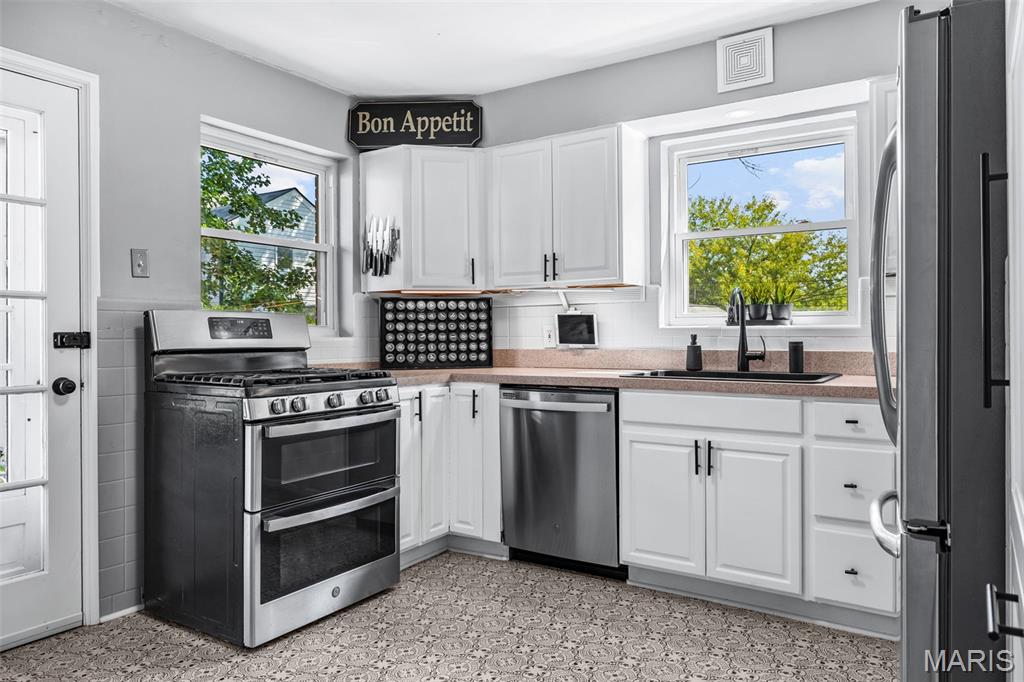 Kitchen with white cabinets, stainless steel appliances, and patterned tile flooring.