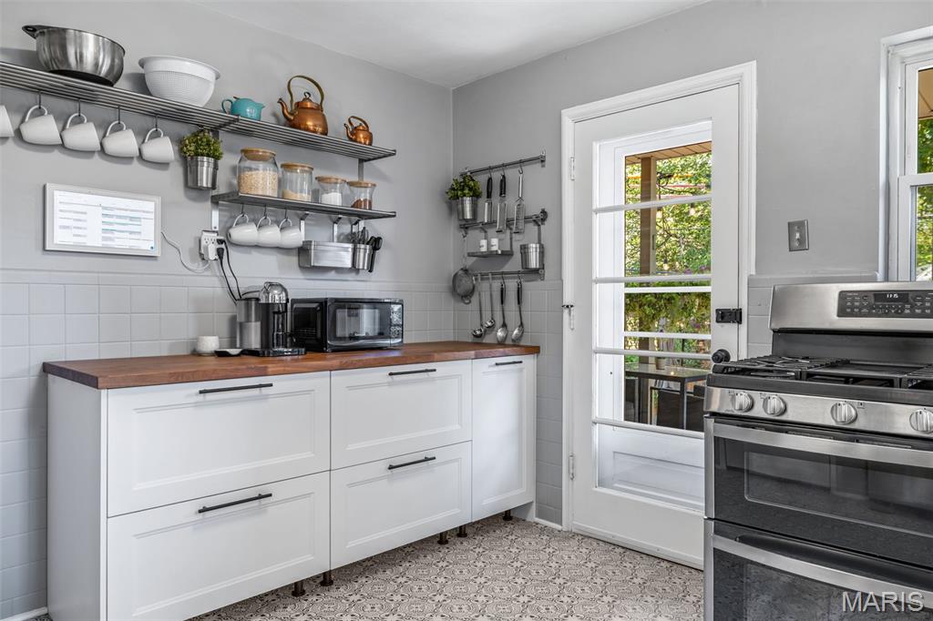 Kitchen with white cabinets, wood countertop, open dish shelves, and a stainless-steel range.