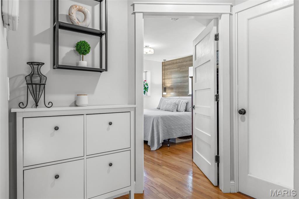 Bedroom visible through an open doorway, with a wood-paneled accent wall and hardwood floors.