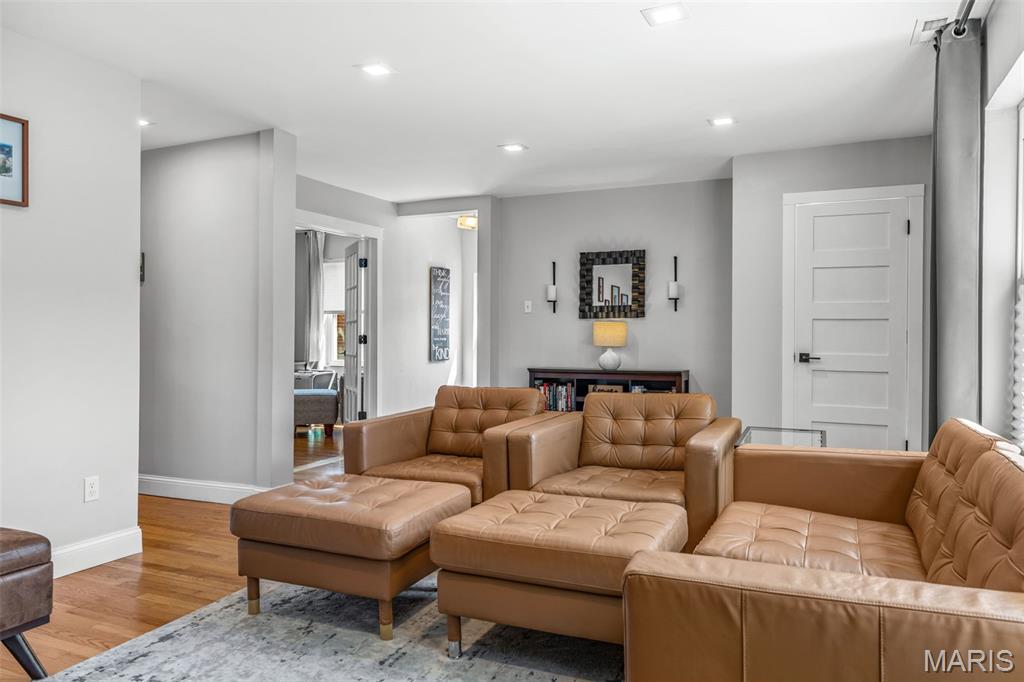 Living room with tan leather sectional seating, hardwood floors, and an opening to an adjoining room.