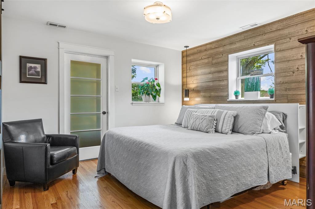 Bedroom with a large gray bed, black leather armchair, hardwood floors, and a wood-plank accent wall.