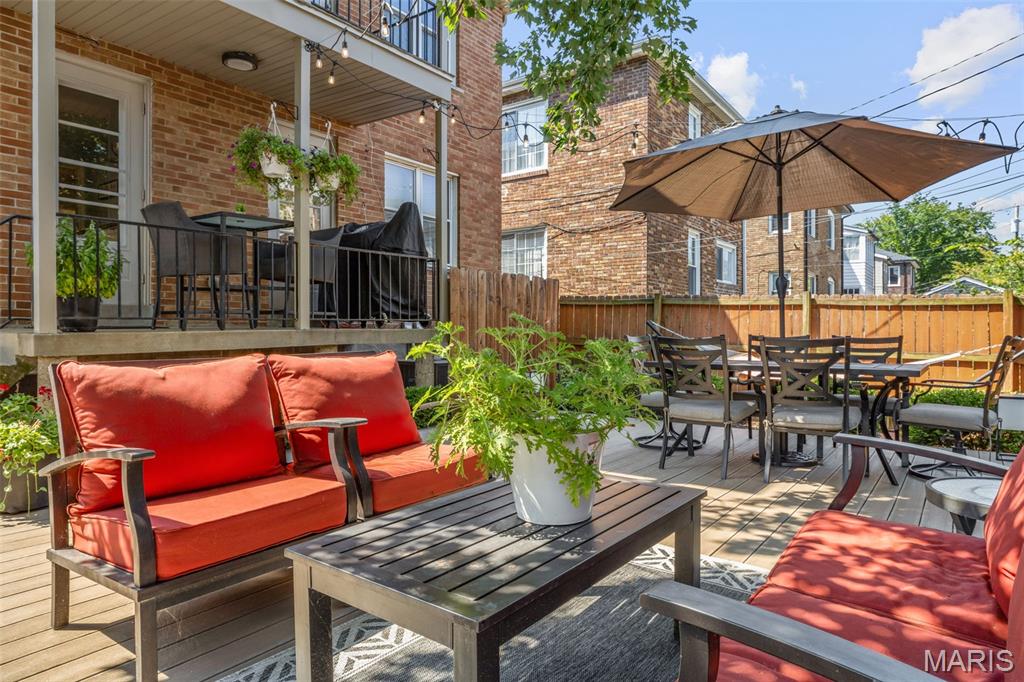 Outdoor deck patio with red-cushioned lounge chairs and umbrella-shaded dining area beside a brick home.