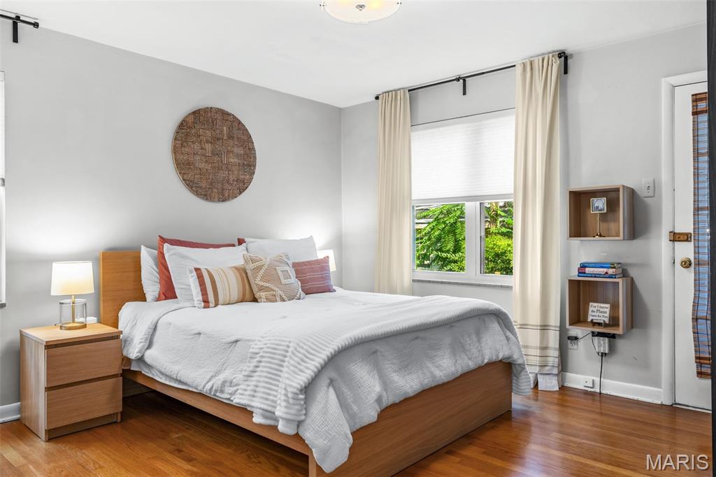 Bedroom with a wood bed, white bedding, striped pillows, and cream curtains beside a bright window.