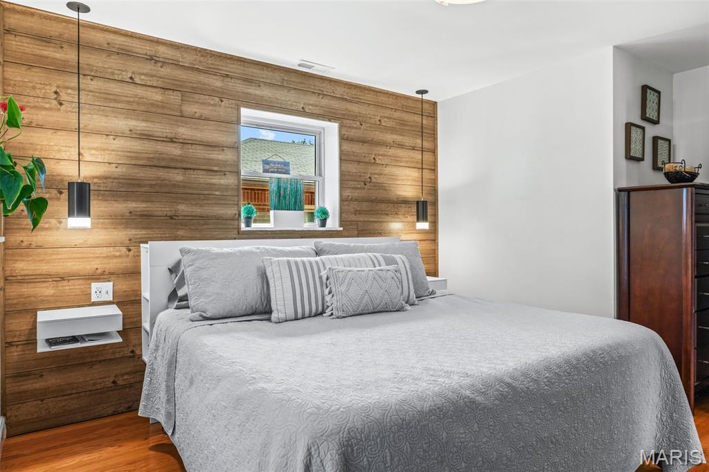 Bedroom with a gray bed against a wood-plank accent wall and pendant lights.